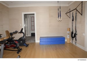This is a photograph of a luxury residential gymnasium featuring multiple pieces of exercise equipment including stationary bikes, gymnastics rings, chin-up bars, and exercise mats. The room appears to be part of a high-end property with professional