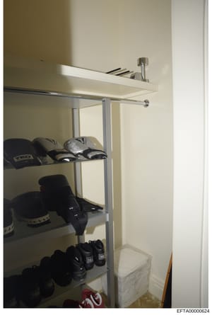 This is a photograph of a closet or storage room containing athletic equipment, primarily boxing gloves and hand wraps. The shelving unit displays multiple pairs of black boxing gloves branded 'Everlast' across three shelves, along with hand wraps an