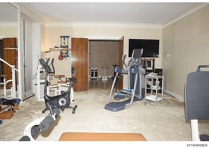 This is a photograph of a well-equipped private gymnasium or fitness room featuring multiple exercise machines, cardio equipment, and training apparatus. The space appears to be located within a residential property and shows a professionally designe