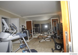 This photograph shows an upscale private gymnasium interior featuring multiple pieces of high-end exercise equipment including treadmills, stationary bikes, and weight machines. The room appears to be located within a luxury property and is equipped 