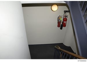 This photograph shows a stairwell landing on the third floor of a building, featuring safety equipment including three fire extinguishers mounted on the wall and a round ceiling light. The image appears to be part of evidence documentation, possibly 