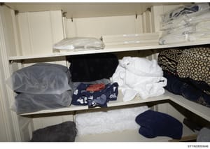 This is a photograph of a white built-in closet or storage cabinet containing various folded linens, towels, and clothing items. The image appears to be evidence documentation from the investigation, likely photographed during a search of one of Epst