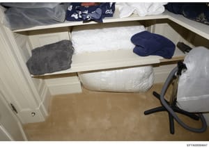 This is a photograph of a residential closet interior showing built-in shelving units with various household items including folded towels, clothing, and storage containers. The image appears to be evidence documentation from a property search or inv