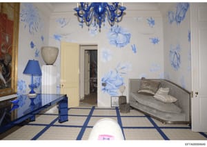 This is a photograph of an elegantly decorated bedroom featuring blue and white chinoiserie-style wall murals, a blue glass chandelier, and luxury furnishings. The room displays high-end interior design with botanical wall paintings, a neutral uphols