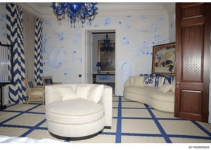 This is a photograph of an elegantly decorated bedroom featuring a sophisticated blue and white color scheme. The room includes custom furnishings, decorative wallpaper with blue botanical motifs, a blue crystal chandelier, geometric patterned curtai