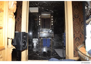 This is a photograph of an upscale bathroom interior, featuring black marble walls, a vanity with illuminated mirror, and ornate decorative elements. The image appears to be evidence documentation from the investigation, likely depicting the interior