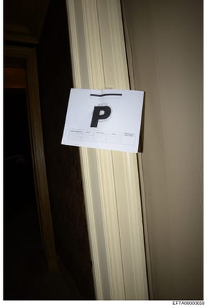 This is a photograph of a white document package or evidence envelope marked with the letter 'P' affixed to a door frame. The package appears to contain forms or documentation with blank fields visible. The photo shows the item in situ as part of the