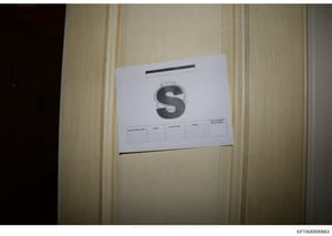 This is a photograph of a white document folder or evidence container labeled with a large letter 'S' and what appears to be a search warrant information form. The label includes fields for search warrant number, agent, contact number, and initials. 