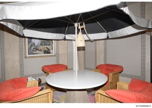 This is an evidence photograph showing an interior/sheltered outdoor space featuring a round white table, wicker chairs with red cushions, and a black-and-white striped umbrella. The space appears to be part of a luxury property with decorative patte