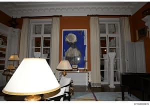 This is a photograph of a formal interior room, likely from one of Epstein's properties, showing an elegantly decorated space with ochre-colored walls, classical architectural details, period furniture, and contemporary artwork. The image documents t
