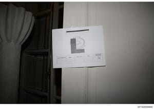 This is a photograph of an evidence documentation card or label affixed to what appears to be a white-painted interior wall or door. The card displays a large letter 'E' with an official seal or emblem, along with a data table for recording search in