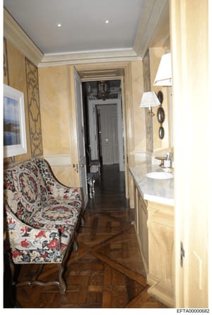This is a photograph of an upscale residential hallway, likely from one of Jeffrey Epstein's properties. The image shows luxurious finishes including travertine or marble wall paneling, decorative wallpaper accents, dark wood herringbone flooring, de