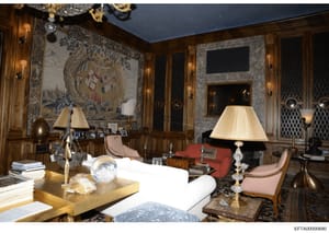 This photograph documents an elegantly appointed interior room featuring high-end furnishings, artwork, and decorative objects. The space contains period furniture, ornate wall tapestries, crystal lighting fixtures, and collectible items arranged thr