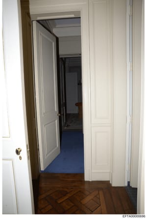 This photograph shows an interior hallway from one of Epstein's properties, featuring cream-colored paneled doors and walls with herringbone wood flooring transitioning to blue carpeting in an adjacent room. The image documents the interior layout an