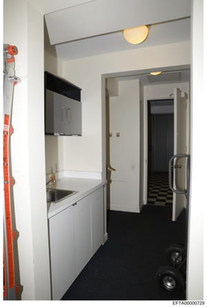 This is an evidence photo showing an interior kitchen and hallway space, likely from one of Jeffrey Epstein's properties. The image depicts white cabinetry, stainless steel appliances, black and white checkered flooring, and various fixtures. The pho