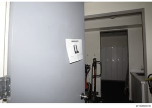 This photograph shows the interior of a room or utility space, featuring a mounted security or access control panel on a light gray wall, along with stored equipment including what appears to be exercise or maintenance equipment. The image provides d