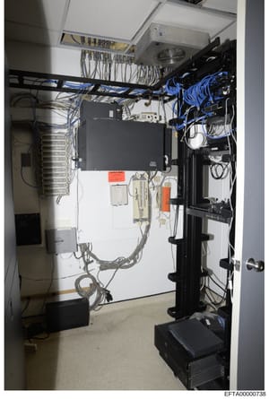 This photograph documents a utility or equipment room containing extensive electrical infrastructure, networking equipment, and cable management systems. The room shows professional-grade installation with organized cabling, power distribution panels