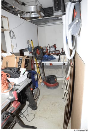 This photograph depicts a basement or storage room containing various maintenance and cleaning equipment, electrical supplies, and tools. The space appears to be from a residential property and contains items such as a floor polisher, extension cords