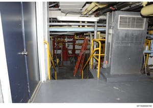 This photograph shows the interior of an industrial mechanical or equipment room, featuring extensive piping infrastructure, HVAC systems, and safety equipment including yellow guardrails and red ladders. The image appears to be from a building inspe