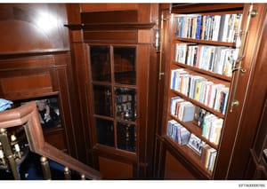 This is a photograph of an interior room with custom wooden cabinetry and glass-fronted shelving containing a collection of books, DVDs, and media. The space appears to be part of a luxury residence, featuring floor-to-ceiling wood paneling and organ