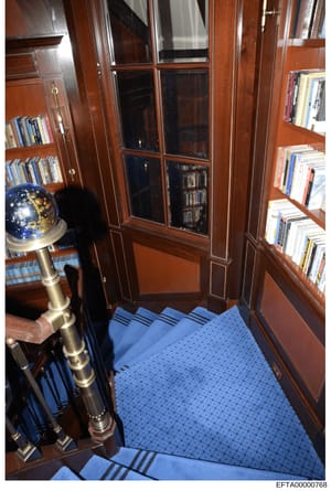 This photograph depicts an interior room with rich mahogany wood paneling, built-in bookshelves, and elegant furnishings. The image shows custom cabinetry, a decorative globe on a brass stand, and a blue patterned carpet, characteristic of a high-end