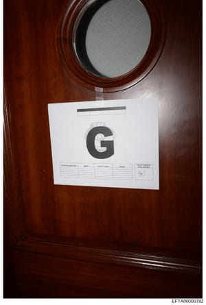 This is a photograph of a search warrant cover sheet affixed to the interior of what appears to be a wooden cabinet or door during a law enforcement search. The sheet displays a large 'G' designation and includes blank fields for recording search per