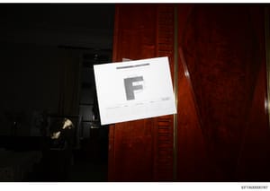 This is an evidence photograph showing a document labeled with the letter 'F' affixed to what appears to be an interior wall or door in a darkened room. The photograph includes a Bates stamp (EFTA00000787) indicating it is part of the formal investig