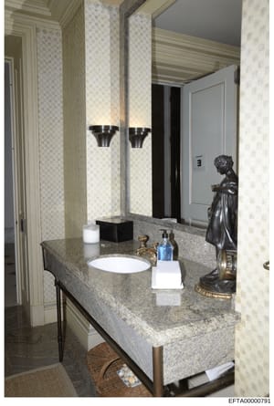 This is a photograph of a luxury bathroom interior, showing a granite countertop with an inset sink, large illuminated mirror, decorative bronze statue, and premium fixtures. The image documents the interior design and appointments of what appears to