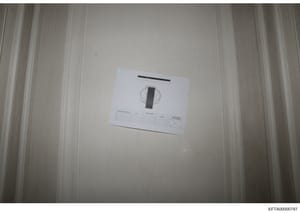 This is a forensic evidence photograph showing a white/cream-colored interior wall or surface with an evidence documentation card or scale marker placed on it. The card contains identification information and measurement references, standard procedur