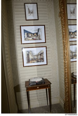 This photograph shows an interior hallway or corridor, likely from one of Epstein's properties, featuring framed architectural renderings and design sketches on the walls, along with a small wooden table displaying what appears to be a Corvette coffe