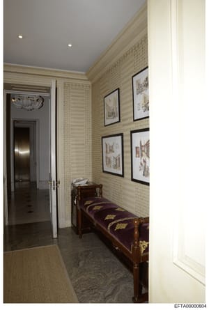 This is a photograph of an elegant, formally decorated hallway or corridor within a residential property. The space features classical architectural elements including ornate crown molding, patterned wallpaper, recessed lighting, and displays of fram
