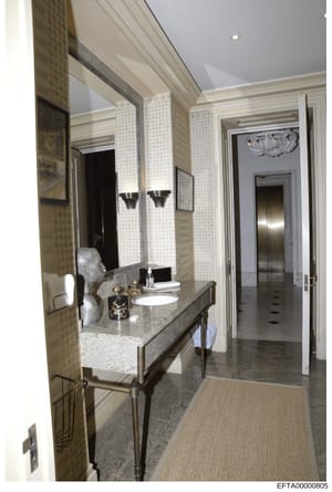 This is a photograph of a high-end bathroom interior, showing a marble vanity with dual sinks, large illuminated mirror, and access to adjacent rooms. The image documents the interior design and finishes of what appears to be a luxury residential pro