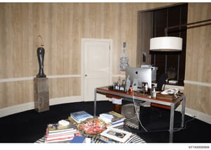 This is an evidence photograph showing an interior office or workspace, likely from one of Jeffrey Epstein's properties. The room features wood-grain wallpaper, a modern desk setup with an Apple computer, decorative art pieces including a guitar-them