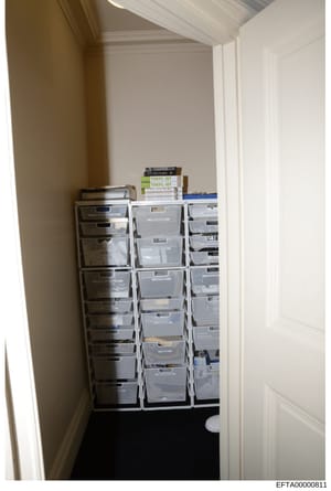 This photograph depicts a residential or office storage closet containing three large stacks of plastic filing/storage boxes organized against the walls. TOEFL IBT test preparation books are visible stacked on top of the boxes. The image appears to b