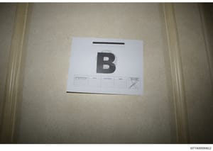 This is an evidence photograph showing a labeled item marked with the letter 'B' placed on a light-colored surface. The item includes a search personnel log form beneath it with columns for Name, Contact Number, and Initials. This appears to be part 