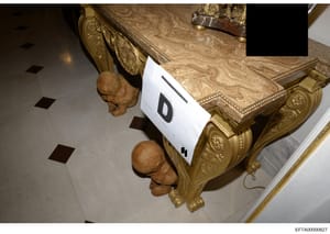 This is an overhead photograph of ornate furniture featuring elaborately carved wooden head sculptures and gilt-decorated table surfaces. The image shows evidence marking (labeled 'D') and appears to be from a property seizure or inventory documentat