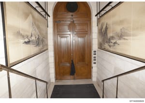 This photograph documents the interior entrance hallway of what appears to be an upscale residential property. The hallway features symmetrically framed landscape artwork on both walls, elegant tile wainscoting, brass handrails, and substantial woode
