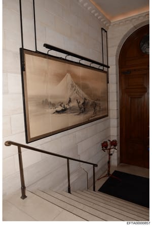 This photograph documents the interior of a stairwell featuring white subway tile walls, a wooden door, metal handrails, and a professionally framed landscape artwork depicting a snow-covered mountain with small figures in the foreground. The image a
