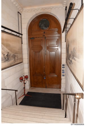 This is a photograph of an upscale residential building's interior entryway or foyer, featuring a distinctive arched wooden double door with a circular transom window. The space shows elegant architectural detailing including decorative framed artwor