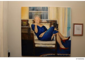 This is a photograph of a framed portrait painting depicting a woman with gray hair wearing a blue dress, reclining on a cream-colored chair in an elegant interior room. The painting shows classical portraiture styling and appears to be displayed on 