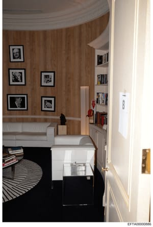 This photograph shows an interior room with wood-paneled walls decorated with black-framed portrait photographs. The room contains modern furnishings including a white sofa, built-in bookshelves, and contemporary décor. The image appears to be eviden