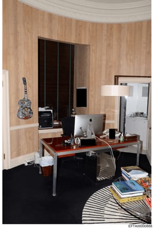 This photograph documents an interior office room, likely from one of Jeffrey Epstein's properties. The room features wood-paneled walls, a desk with computer equipment, decorative items including a guitar art piece, and various furnishings. The imag