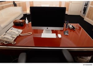 This photograph shows a well-appointed executive office space featuring a polished red-wood desk with modern computer equipment, telecommunications devices, and office supplies. The image appears to be evidence documentation from a property search or