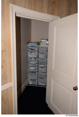 This is an evidence photograph showing the interior of a small closet or storage space containing multiple plastic storage drawers organized in two columns. Several books and documents are stacked on top of the drawer units, including materials label
