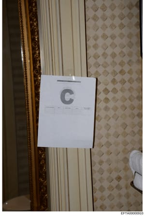 This is a photograph of an evidence marker labeled 'C' placed against a wall or door in an interior room. The marker appears to be part of a systematic evidence documentation process, with a table visible on the marker for recording details. The back