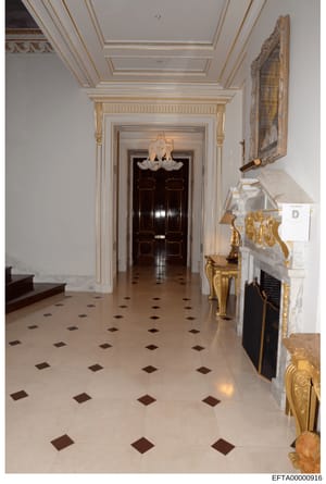 This is a photograph of an elaborate entrance hallway or foyer featuring high-end neoclassical architectural details, including coffered ceilings with gold leaf trim, ornate moldings, marble flooring with geometric inlays, and luxury furnishings. The