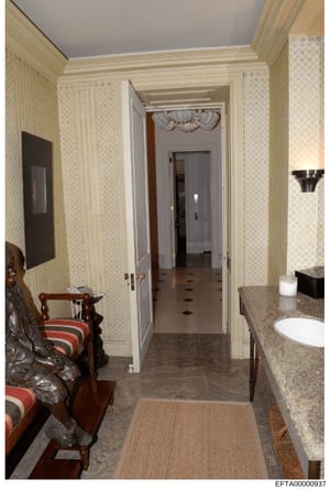This is a photograph of an elegantly decorated bathroom interior, featuring cream and beige wallpaper, marble countertops, designer fixtures, and a view into an adjoining hallway. The image appears to be documentation of property interior design or r