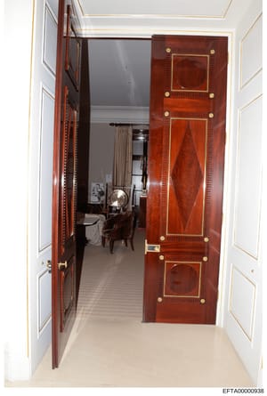 This is an evidence photograph showing the interior of a high-end residential property, depicting an entryway with ornate mahogany or similar fine wood double doors featuring inlaid panels and brass hardware. The photo captures the threshold into wha