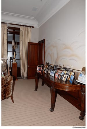 This photograph documents the interior of what appears to be a bedroom in one of Jeffrey Epstein's properties, showing ornate furniture, decorative elements, and personal items displayed on a dark wooden console table. The room features high-end furn