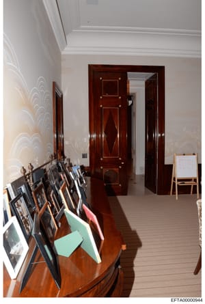 This is an evidence photograph showing an interior room with elegant furnishings and decorative elements. The image depicts a hallway or passage with dark wooden doors featuring decorative hardware, white crown molding, patterned wallpaper, and a col
